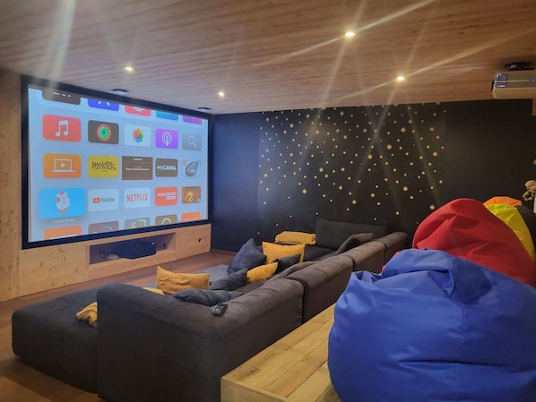 A modern living room with a large screen displaying streaming services, a cozy sofa, bean bags, and a starry wall decoration.
