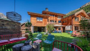 Una cabaña de madera con un patio amplio, mobiliario exterior y un paisaje de montañas.
