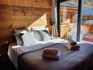 A wooden cabin-style bedroom with a large bed, pillows, and a view of the outside.