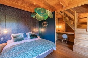 A bedroom with a wooden ceiling, a bed with a floral bedspread, a wall with a textured pattern, and a staircase.