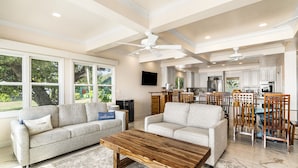 A spacious living room with a large wooden coffee table, two grey sofas, and a dining area with wooden chairs. - Dolphin Manor: Stunning Oceanfront Home w/Pool, Spa, A/C, Private Lanai (Kailua Kona)