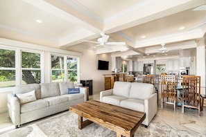 A spacious living room with a large wooden coffee table, two grey sofas, and a dining area with wooden chairs.