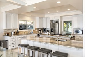 A modern kitchen with white cabinetry, a large island with bar stools, stainless steel appliances, and a view of the outdoors.