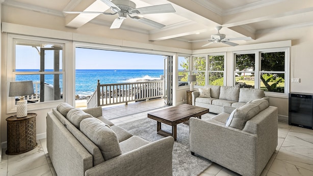 A spacious living area with a large window overlooking the ocean, a ceiling fan, and a modern sofa set. - Dolphin Manor: Stunning Oceanfront Home w/Pool, Spa, A/C, Private Lanai (Kailua Kona)