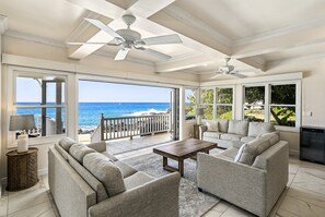 Ein großzügiger Wohnbereich mit großem Fenster zum Meer, Deckenventilator und einer modernen Sofagarnitur.