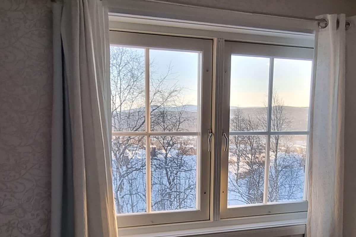 Una habitación con cama, ventana con cortinas y vistas a un paisaje nevado.