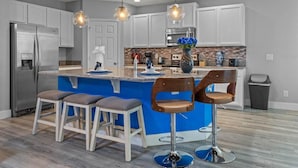 Cozinha moderna com ilha central, banquetas, eletrodomésticos de aço inoxidável e iluminação pendente.