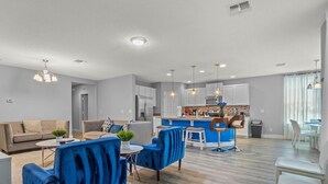 Uma sala moderna com um sofá azul, uma cozinha com uma ilha azul e uma área de jantar com mesa e cadeiras.