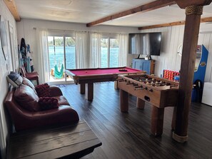 Una sala con mesa de billar, mesa de futbolín, sofá de cuero y televisor.