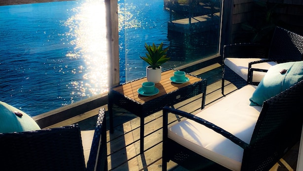 A balcony with a view of a lake, a glass railing, and outdoor furniture including a sofa and chairs.