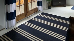 A room with a large sliding glass door, a ceiling fan, a dark wooden dresser, a potted plant, and a striped rug.