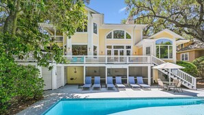Ein zweistöckiges Haus mit Pool, Sitzgelegenheiten im Freien und einer Treppe zu einem Balkon.