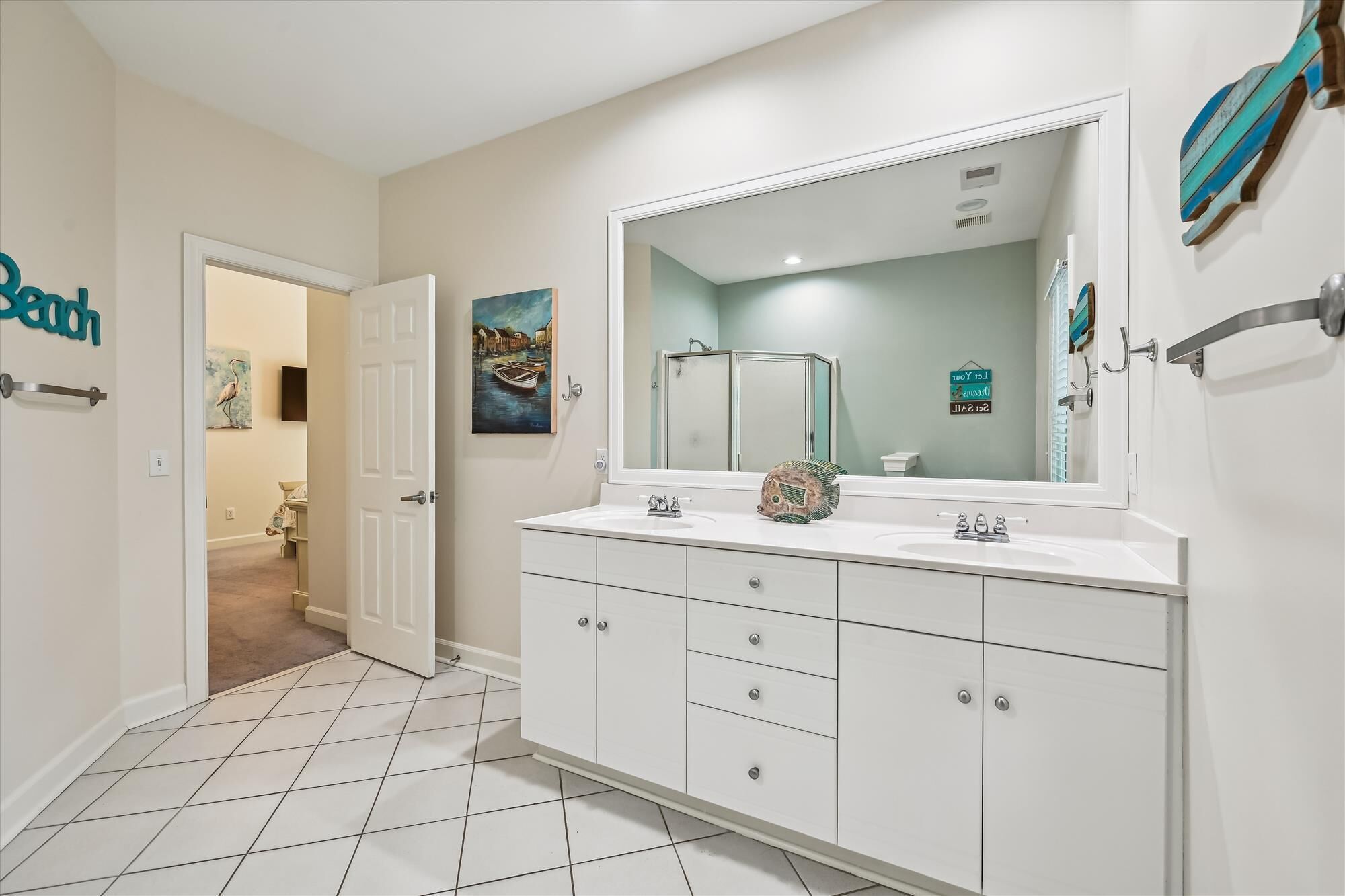 A bathroom with a white vanity, a large mirror, and a door leading to another room.