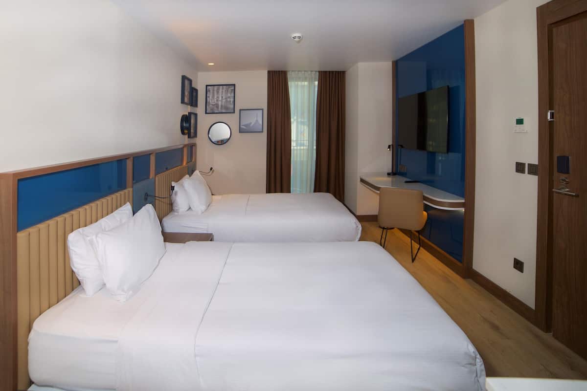 A hotel room with two beds, a desk, a chair, a television, and a mirror.