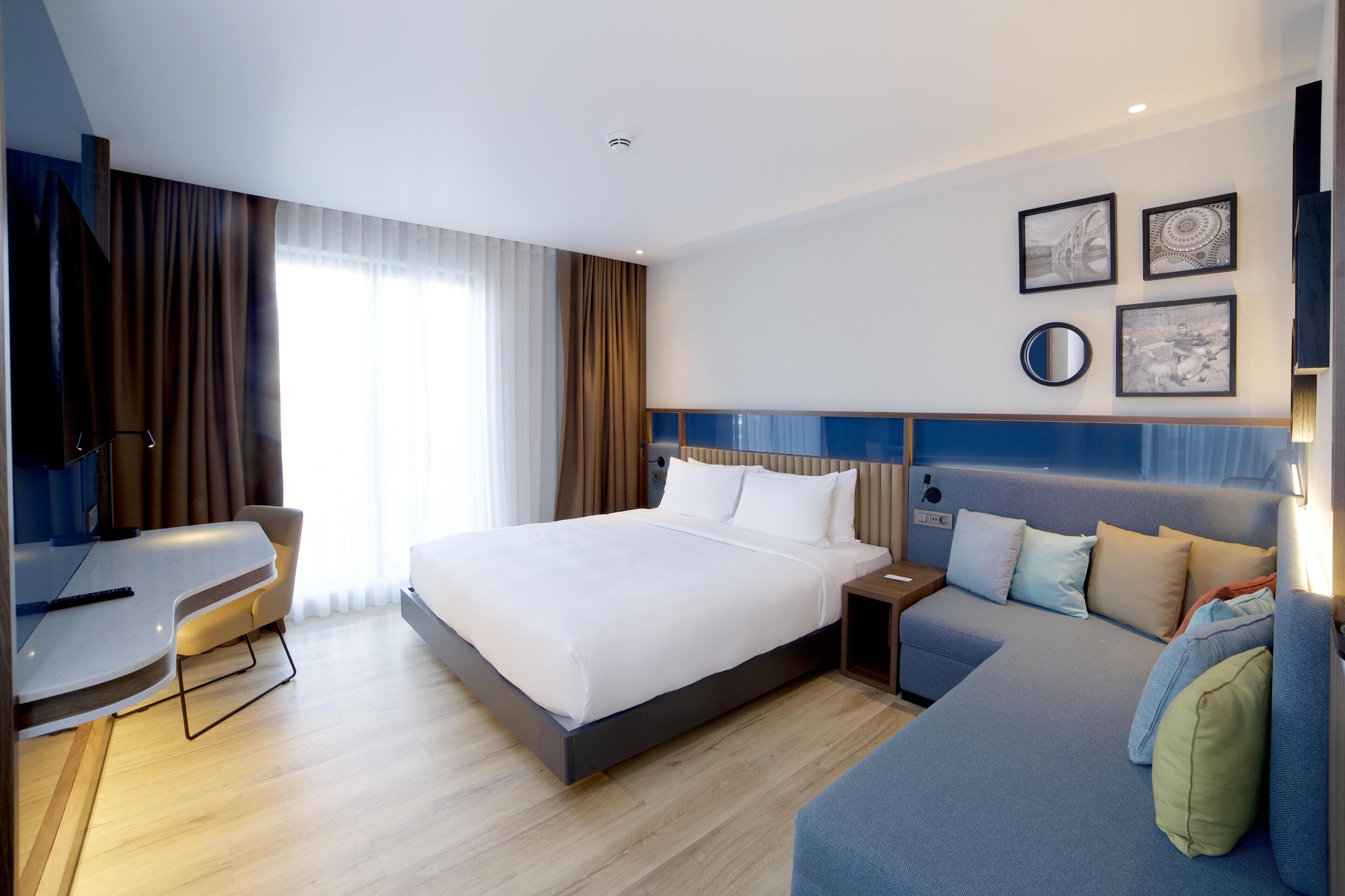 A modern hotel room with a large bed, a sofa, a desk, and a TV.