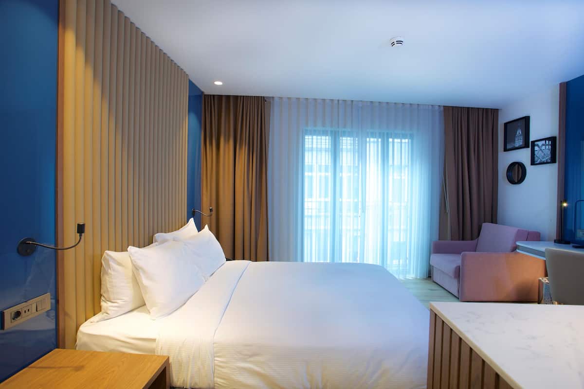A hotel room with a large bed, a desk, a chair, a sofa, and a window with curtains.