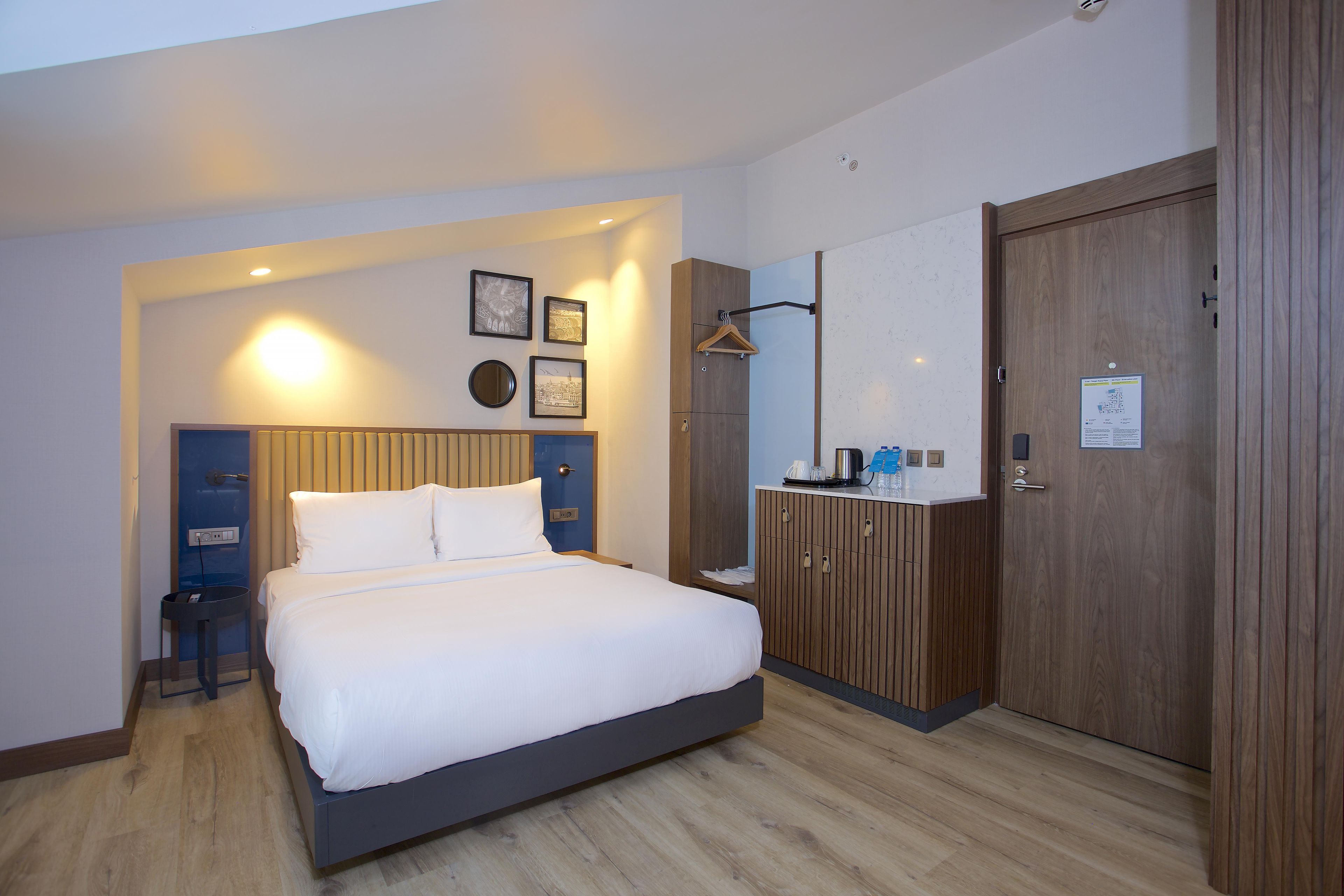 A hotel room with a bed, wardrobe, bedside table, and wall-mounted artwork.