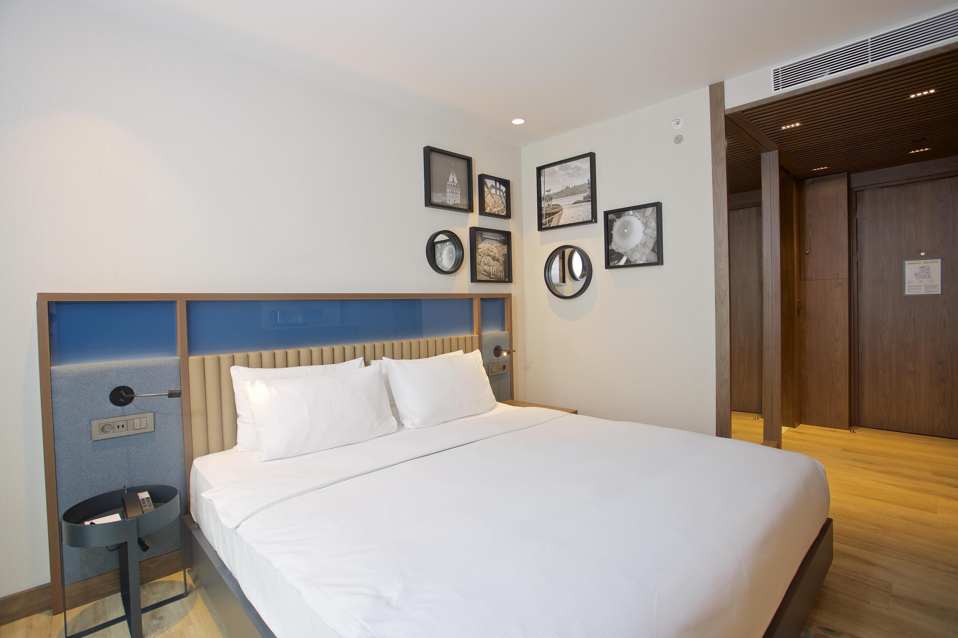 Ein Hotelzimmer mit einem großen Bett, einem Nachttisch mit Telefon und einer Wand mit gerahmten Bildern.