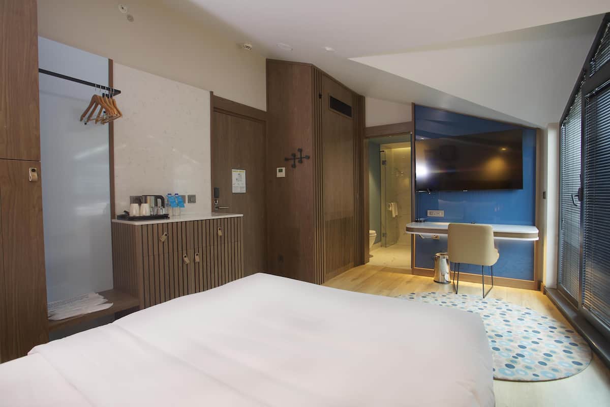 A modern hotel room with a bed, wardrobe, vanity, and a TV.