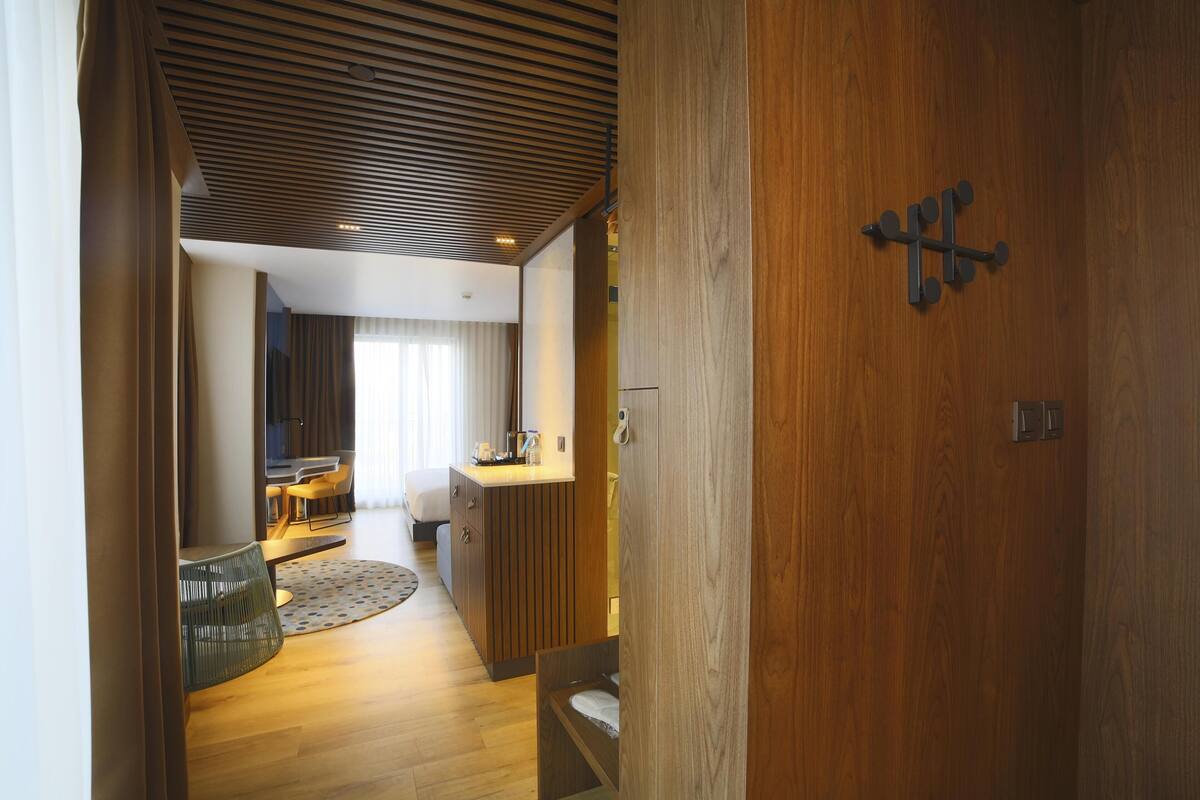 A modern hotel room with a wooden ceiling, a bed, a desk, and a small seating area.
