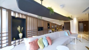 En moderne hotellobby med en stor sofa, runde borde og en dekorativ væg med planter.