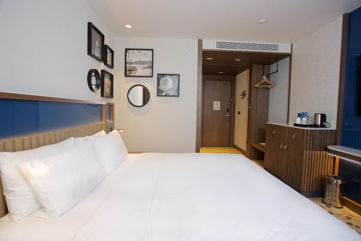 A hotel room with a large bed, a wardrobe, a mirror, and a small kitchenette area.