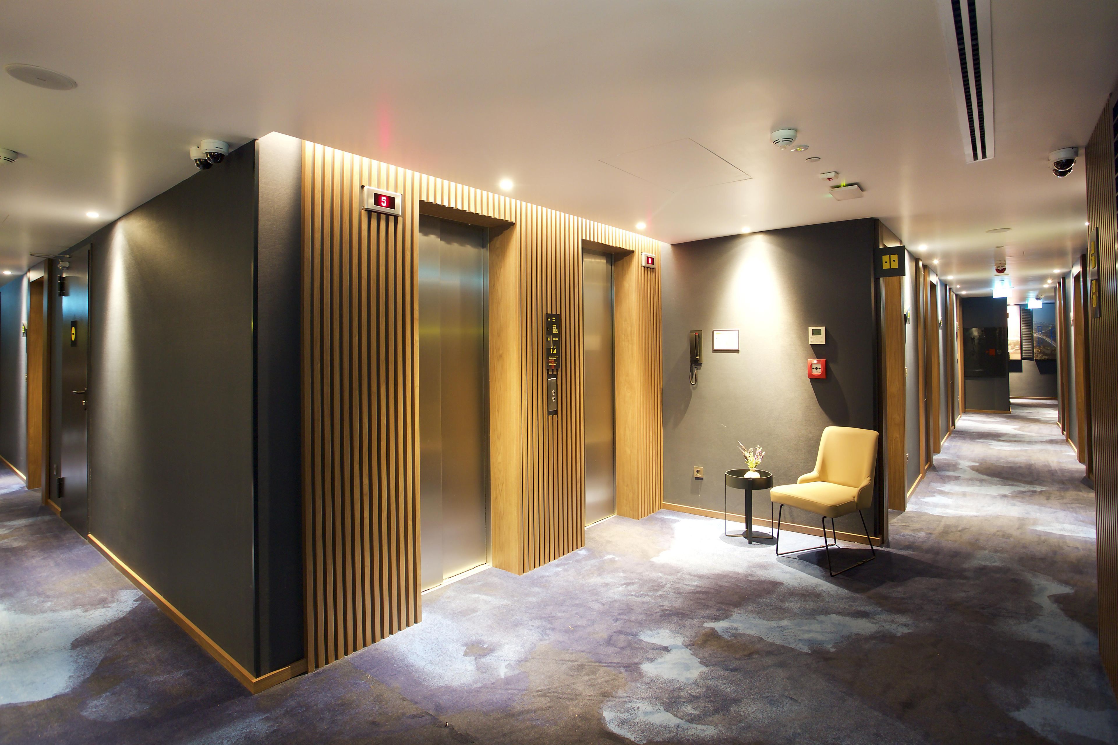 A hotel lobby with a modern elevator, a reception desk, and a seating area.