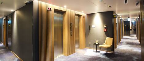 A hotel lobby with a modern elevator, a reception desk, and a seating area.