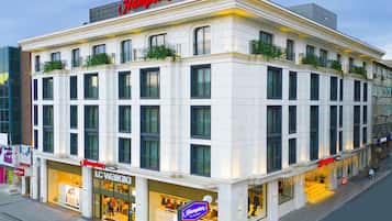 Un hotel con un llamativo letrero de Hampton, varias tiendas, incluyendo LC Waikiki, y un estilo arquitectónico clásico con balcones.