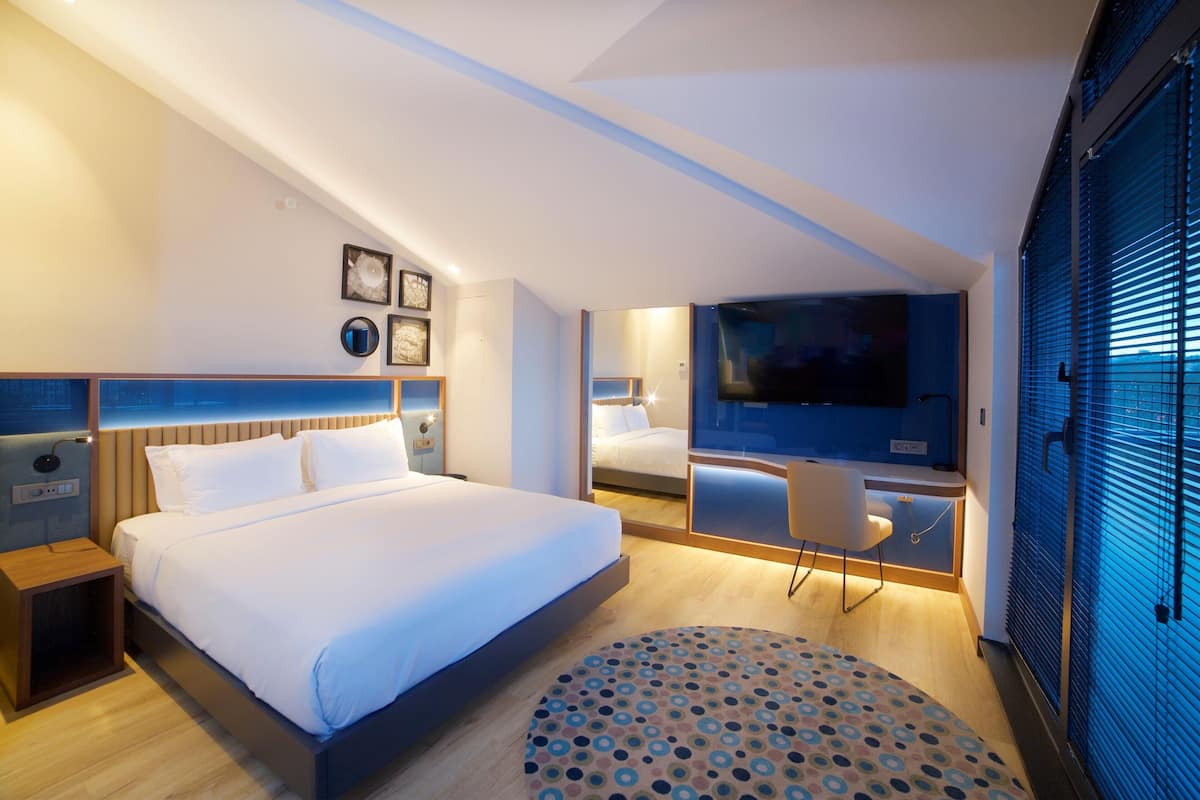 A modern hotel room with a large bed, a desk, and a TV.
