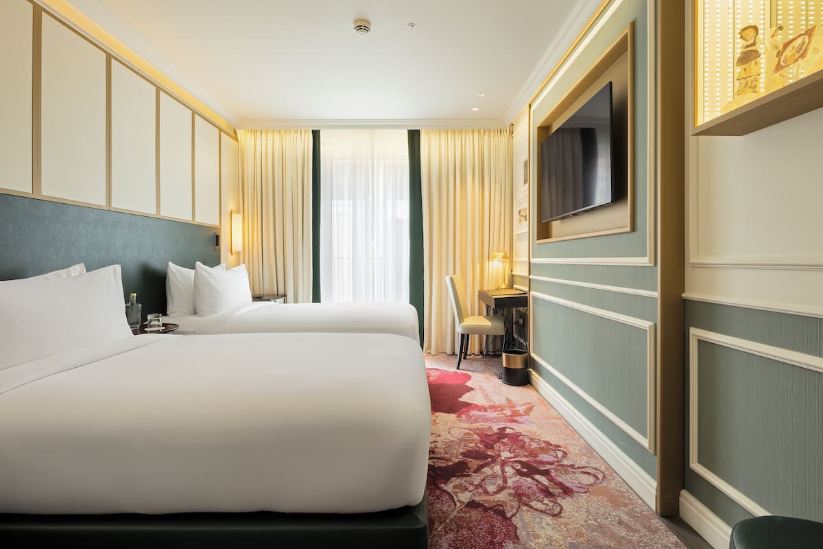 Habitación de hotel con una cama grande, un escritorio, una silla, un televisor y una ventana con cortinas.