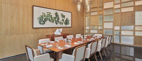 Une salle de conférence avec une longue table, des chaises, une œuvre d’art encadrée et un mur en bois doté d’une cloison en verre.