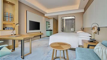 Una habitación de hotel moderna con una cama grande, un escritorio, un televisor y un sofá.