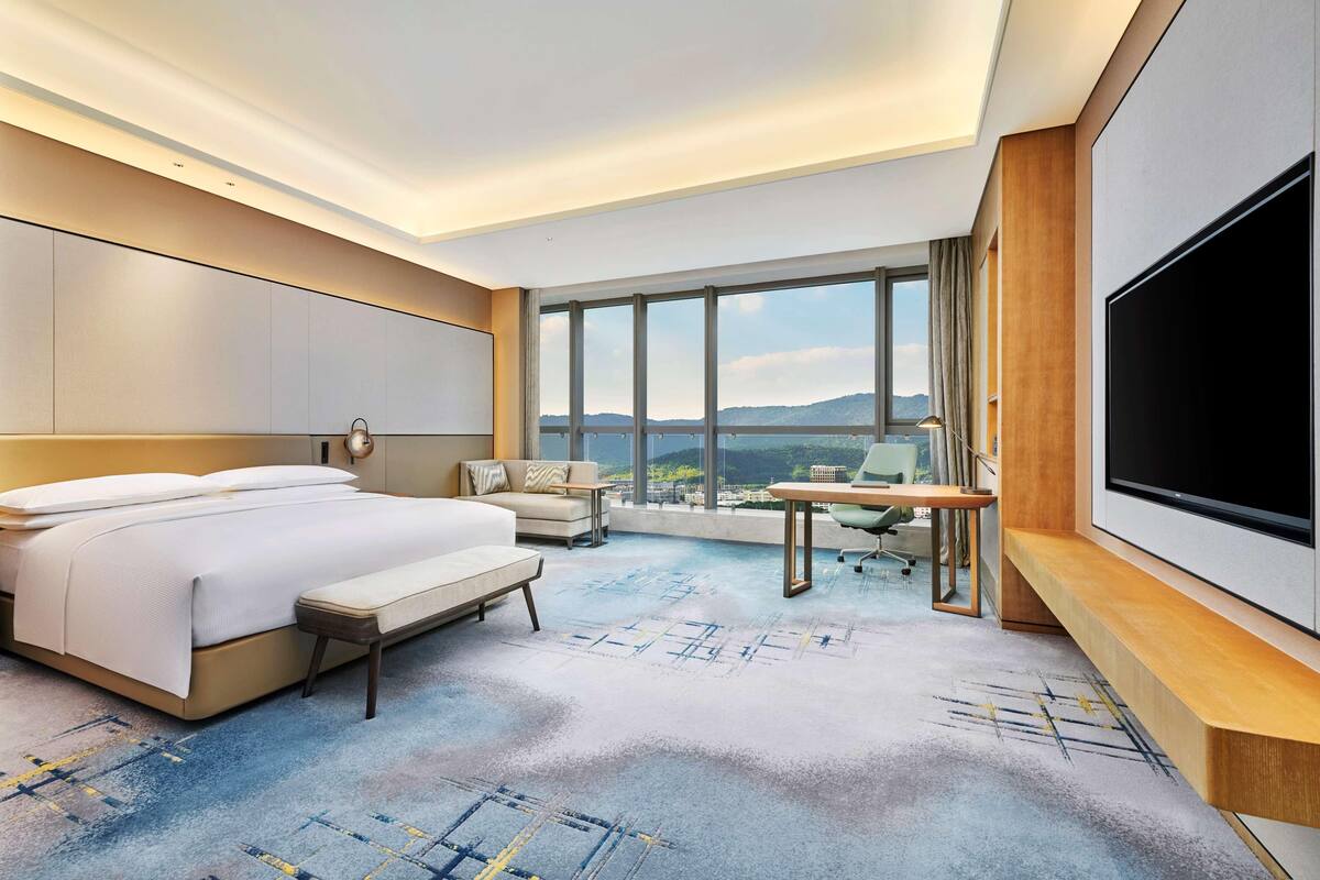 Ein modernes Hotelzimmer mit einem großen Bett, einem Schreibtisch, einem Fernseher und Blick auf die Stadt.