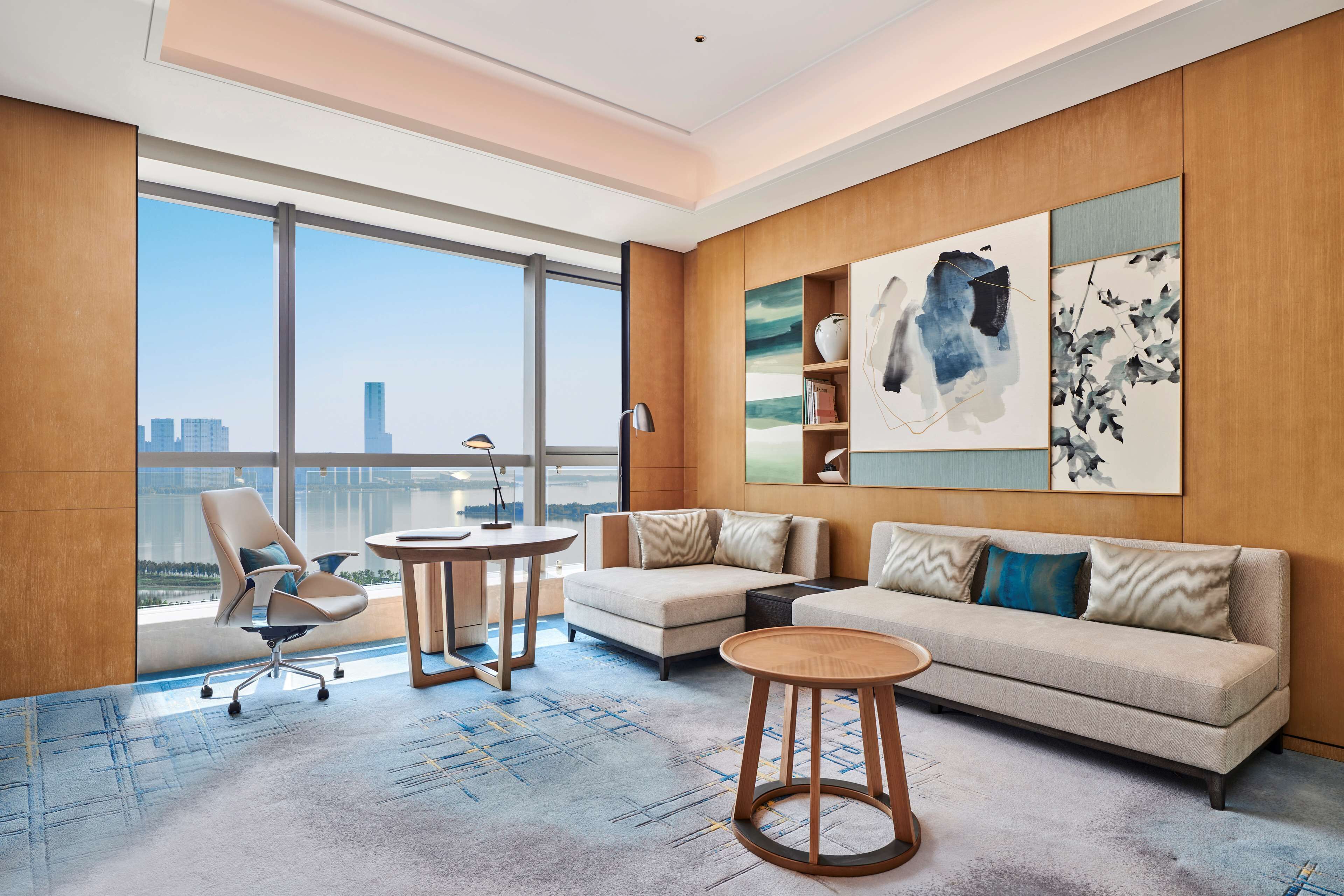 Een moderne hotelkamer met een groot raam, een bank, een stoel, een klein tafeltje en kunst aan de muur.