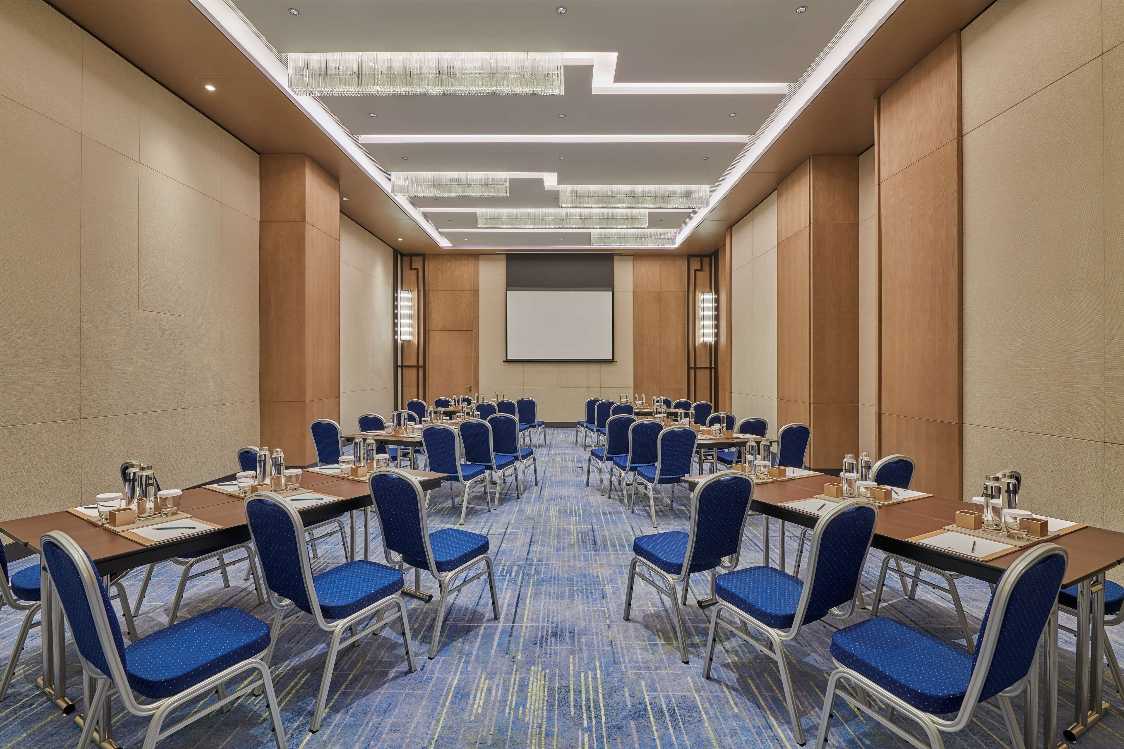A conference room with a long table, blue chairs, and a projector screen.