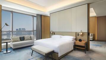 Ein modernes Hotelzimmer mit einem großen Bett, einer Couch, einer Bank, einem Nachttisch und Blick auf die Stadt.