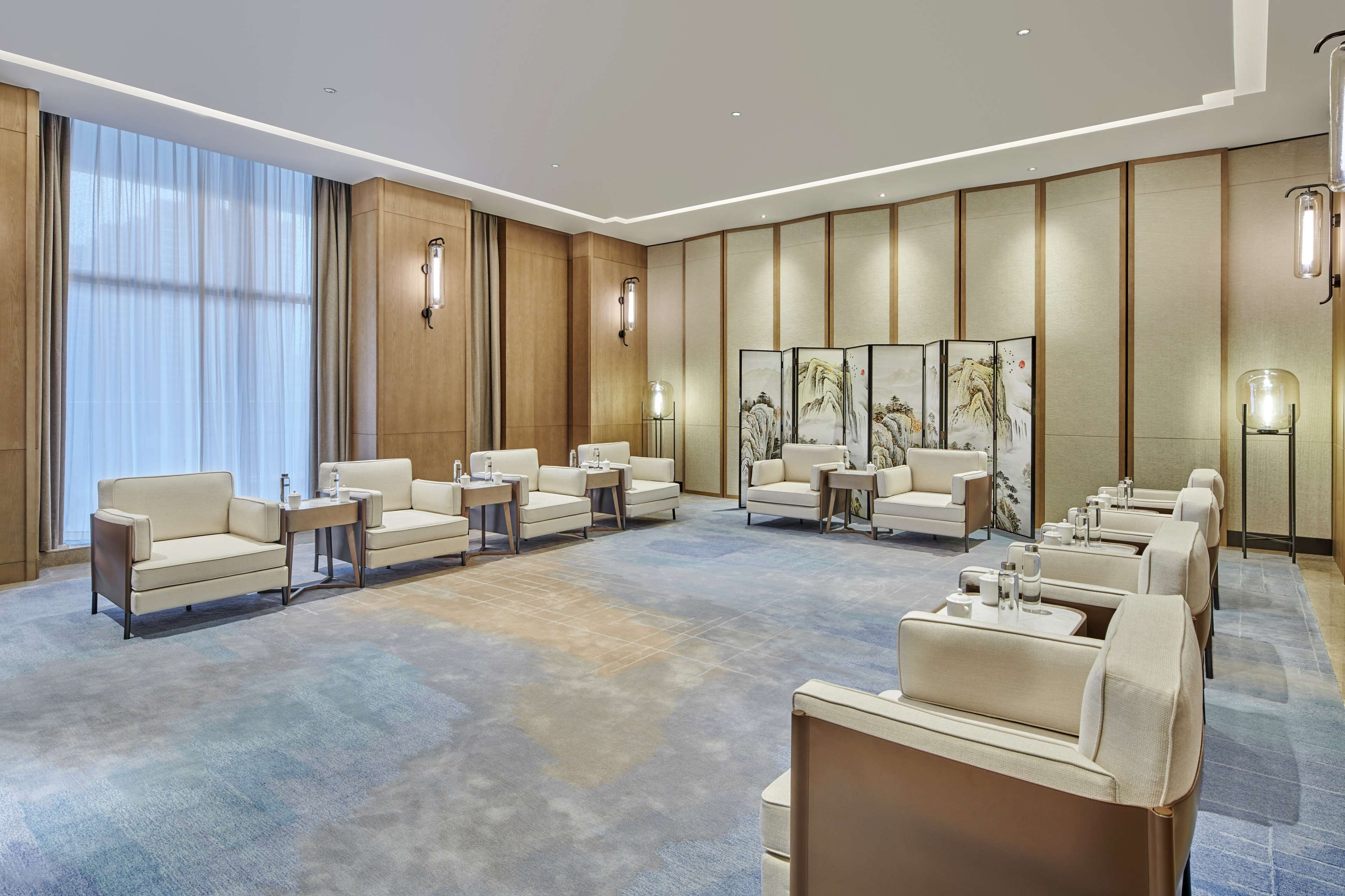 A spacious hotel lobby with multiple seating areas, including sofas and armchairs, arranged around a central coffee table.