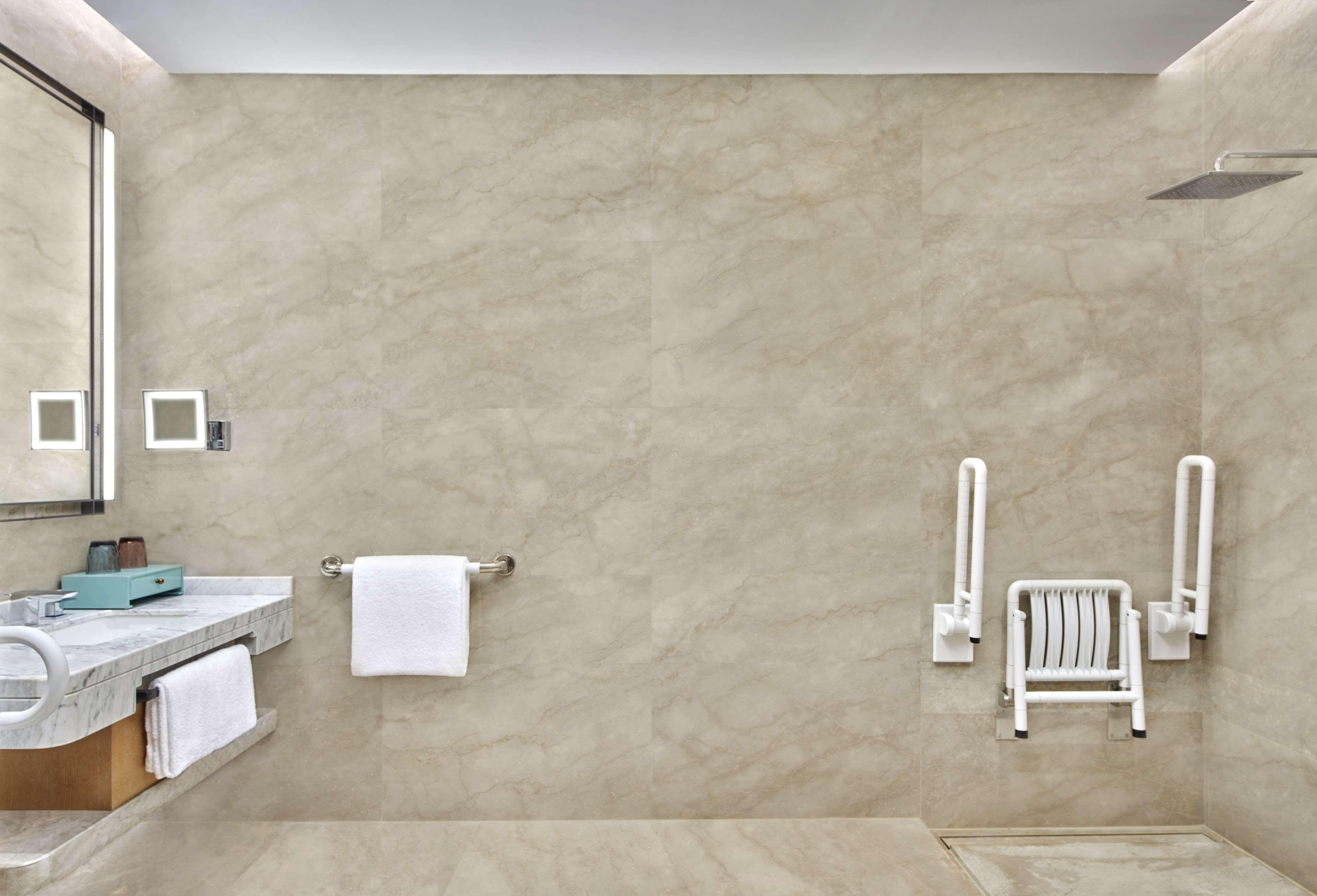 A modern bathroom with a marble wall, a sink with a mirror, a towel rack, and a shower area with a white chair.