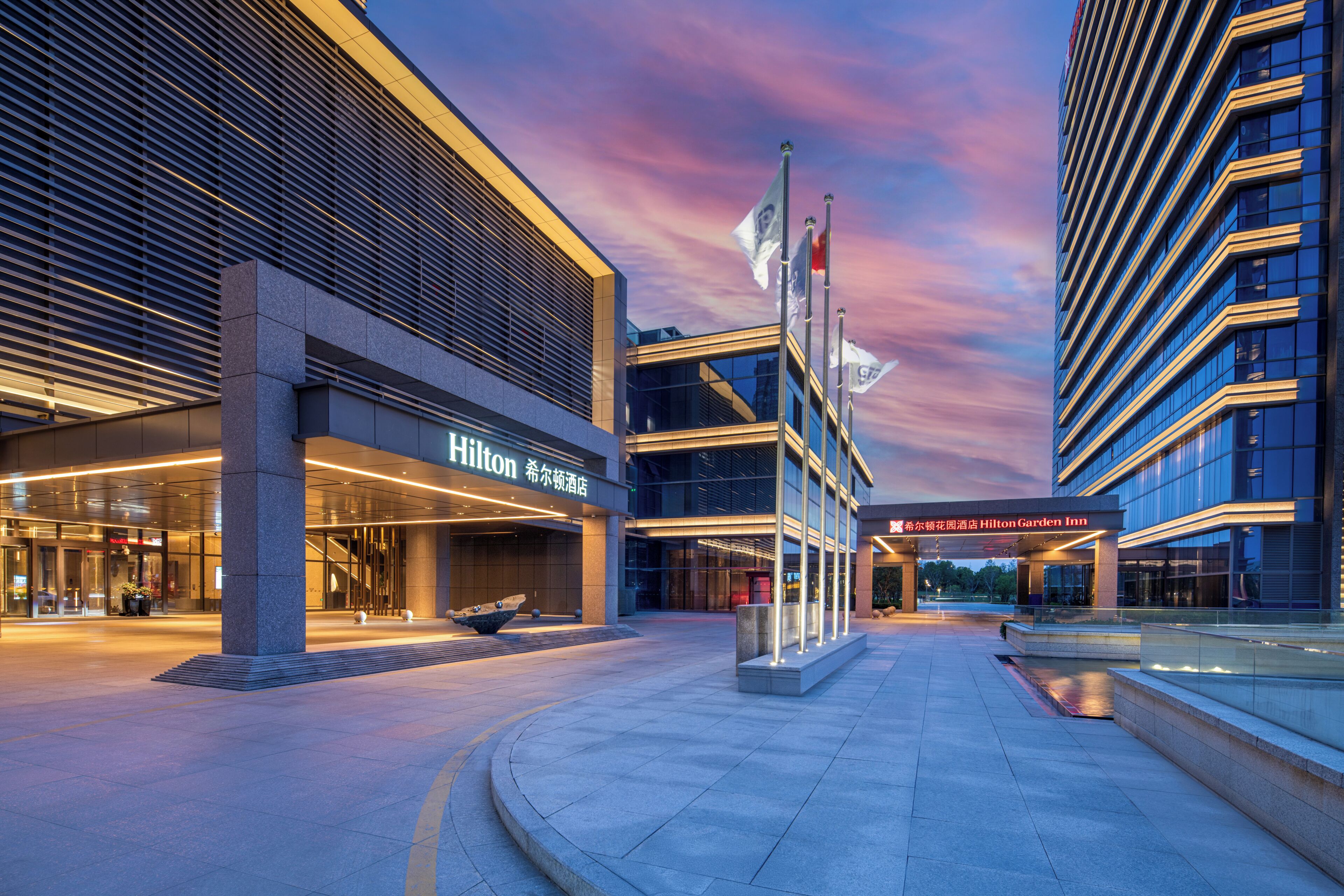 A modern hotel entrance with a glass facade, a large pillar, and a sign for Hilton Garden Inn.