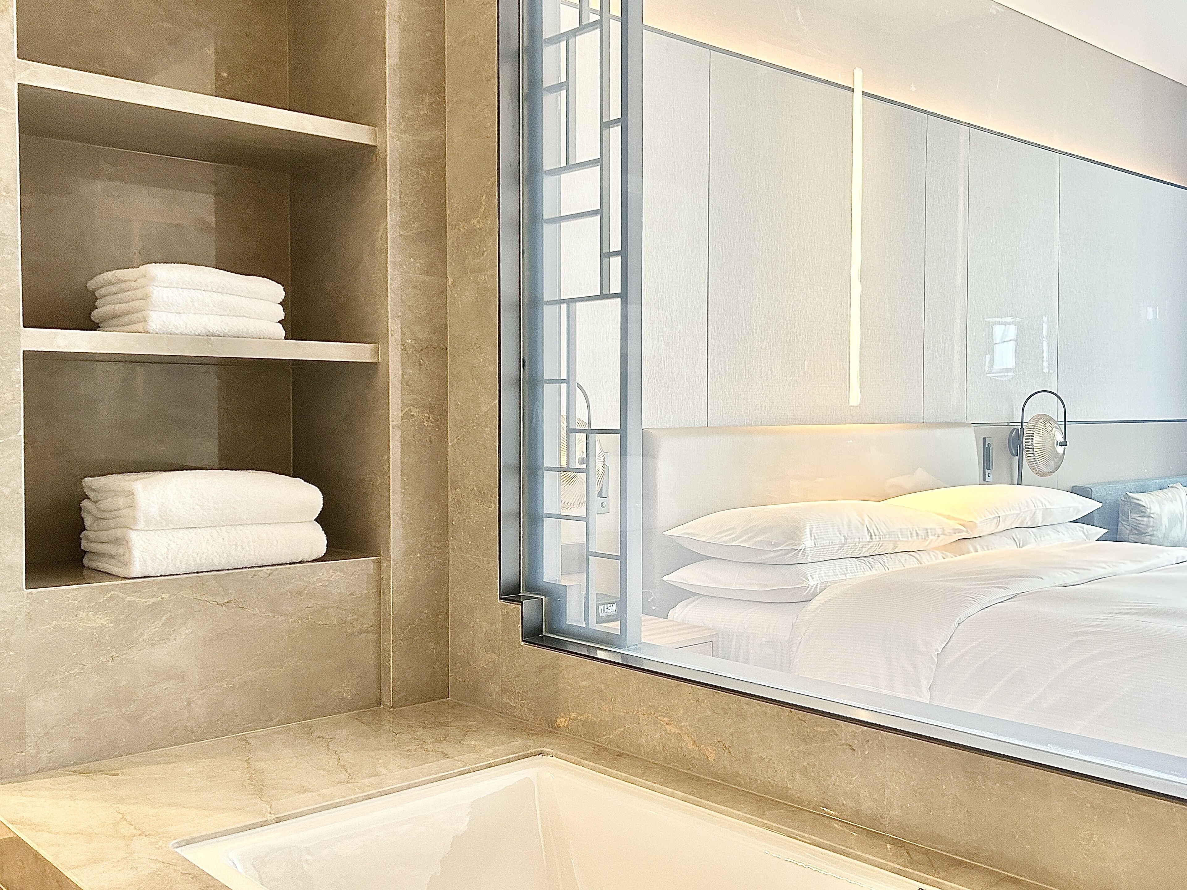 A modern bathroom with a large mirror, a built-in shelf with folded towels, and a visible shower area.