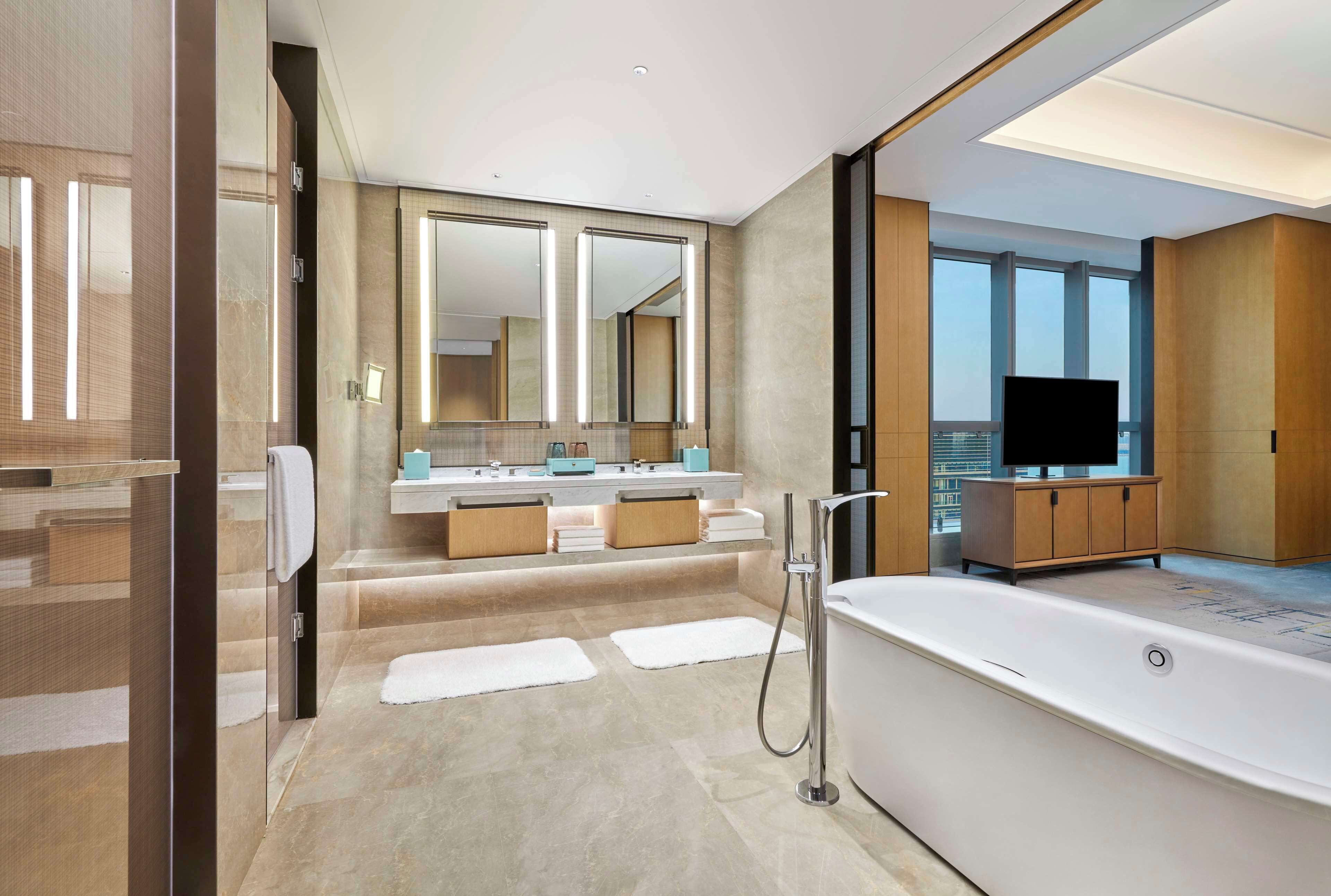 Ein modernes Badezimmer mit einer großen Badewanne, einem Waschtisch mit Spiegel und Blick auf die Stadt.
