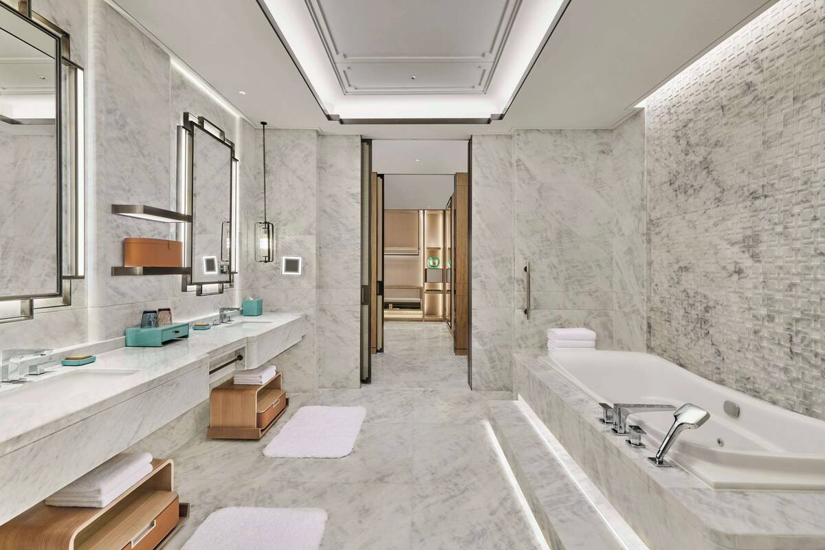 Ein modernes Badezimmer mit Marmorboden, einer großen Badewanne und einem Waschtisch mit Spiegel und Waschbecken.