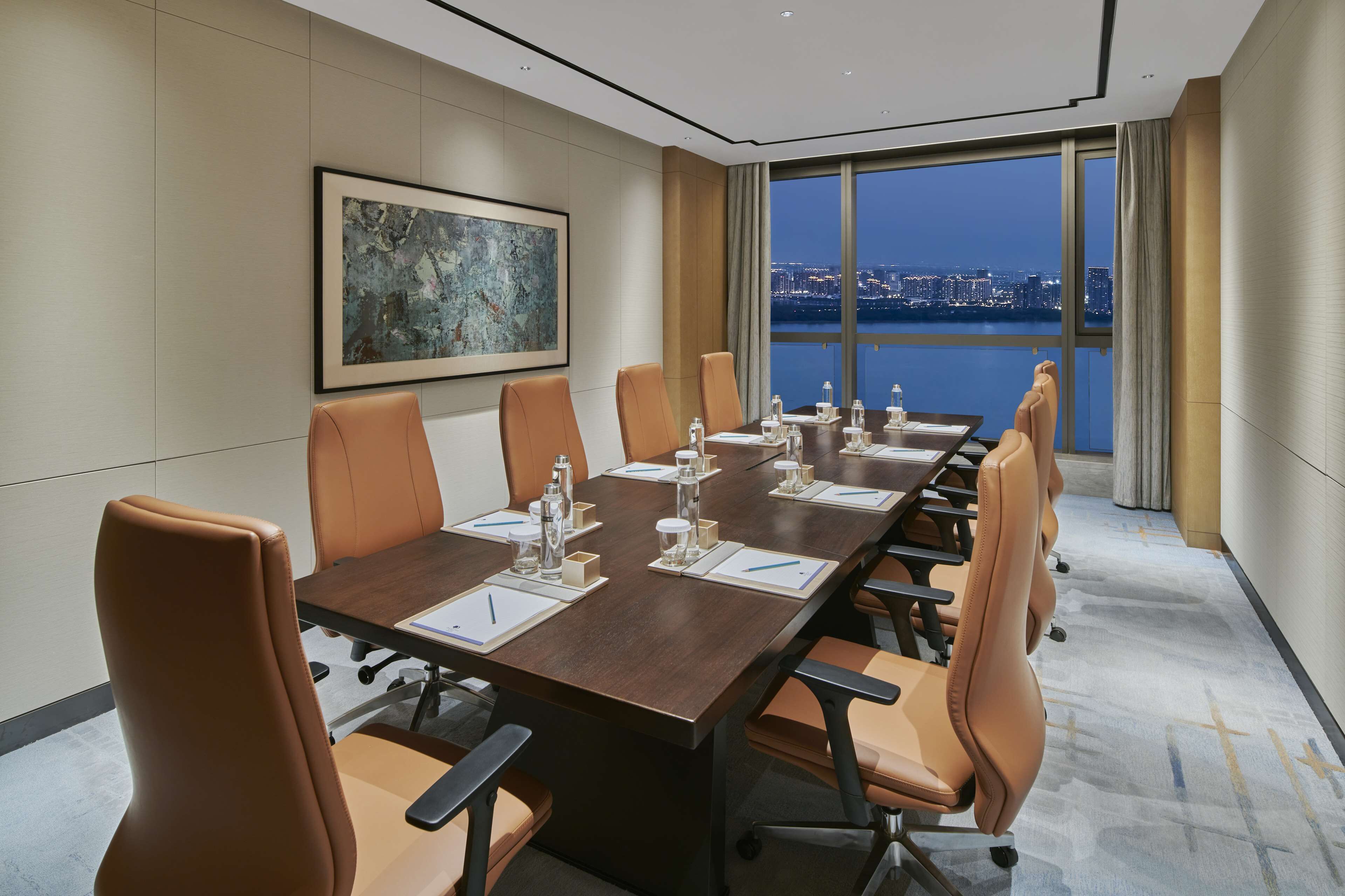 A conference room with a long table, leather chairs, and a city view through large windows.