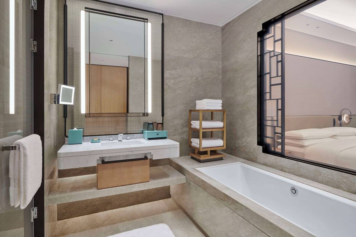 Ein modernes Badezimmer mit einem großen Spiegel, einer Badewanne und einer Holzablage mit Handtüchern.