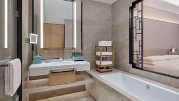 A modern bathroom with a large mirror, a bathtub, and a wooden shelf with towels.