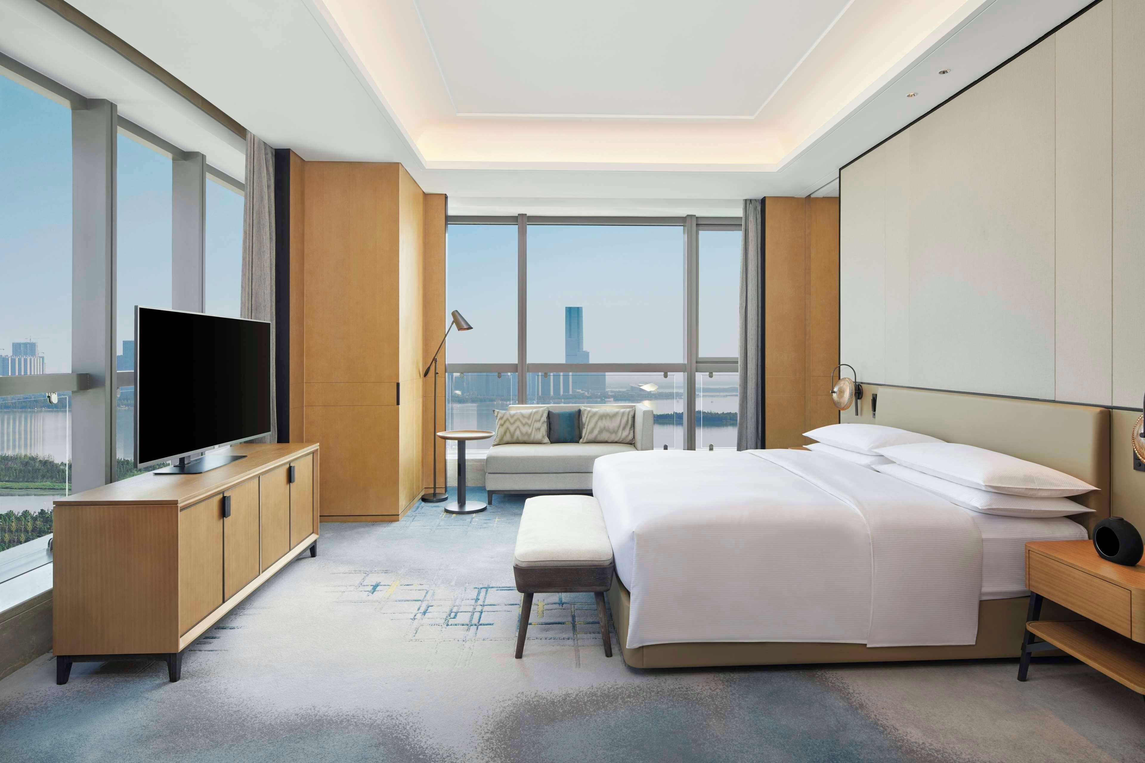 A modern hotel room with a large bed, a TV on a wooden cabinet, a small table, and a sofa.