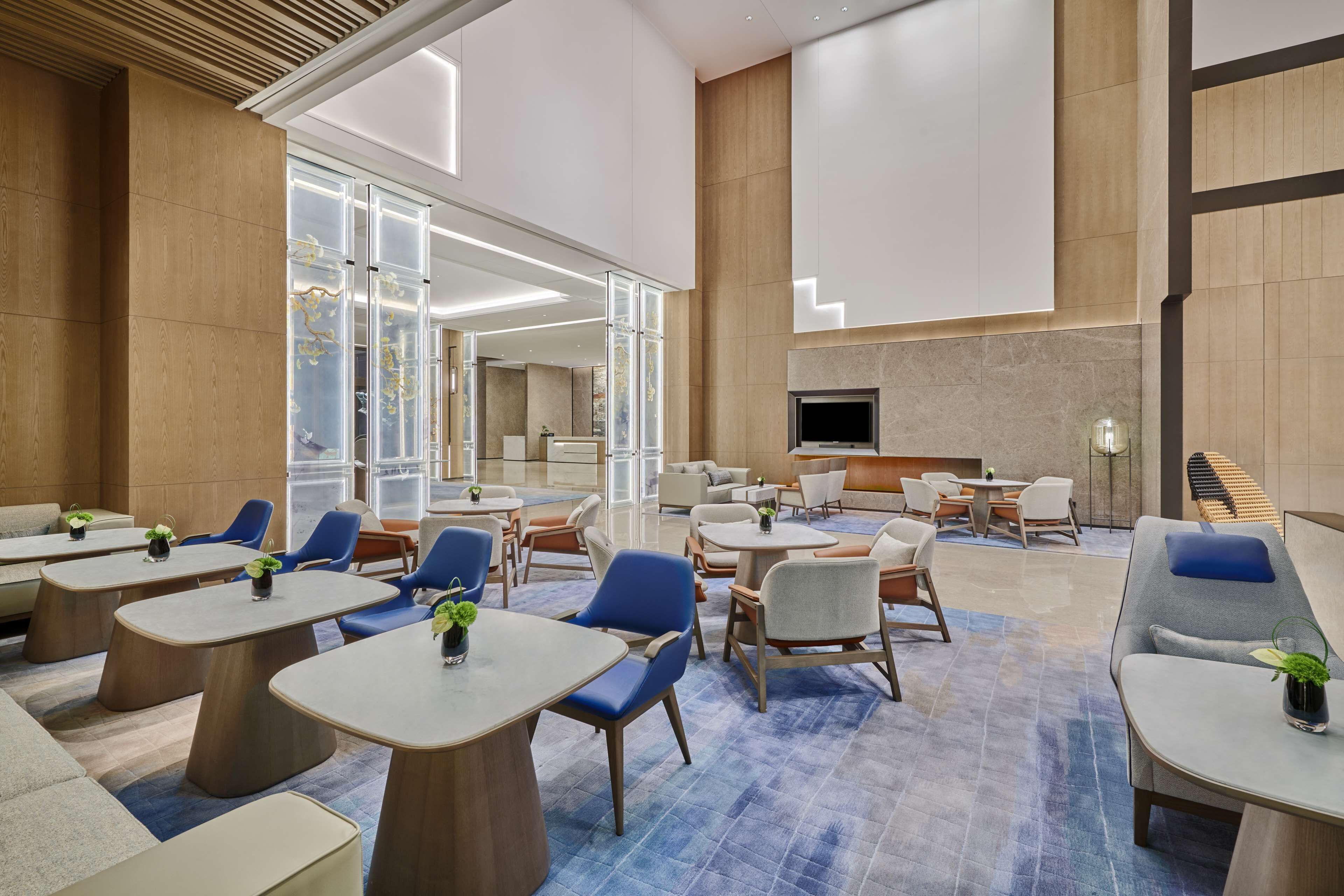 A spacious lobby with multiple seating areas, including tables and chairs, and a large TV screen mounted on the wall.