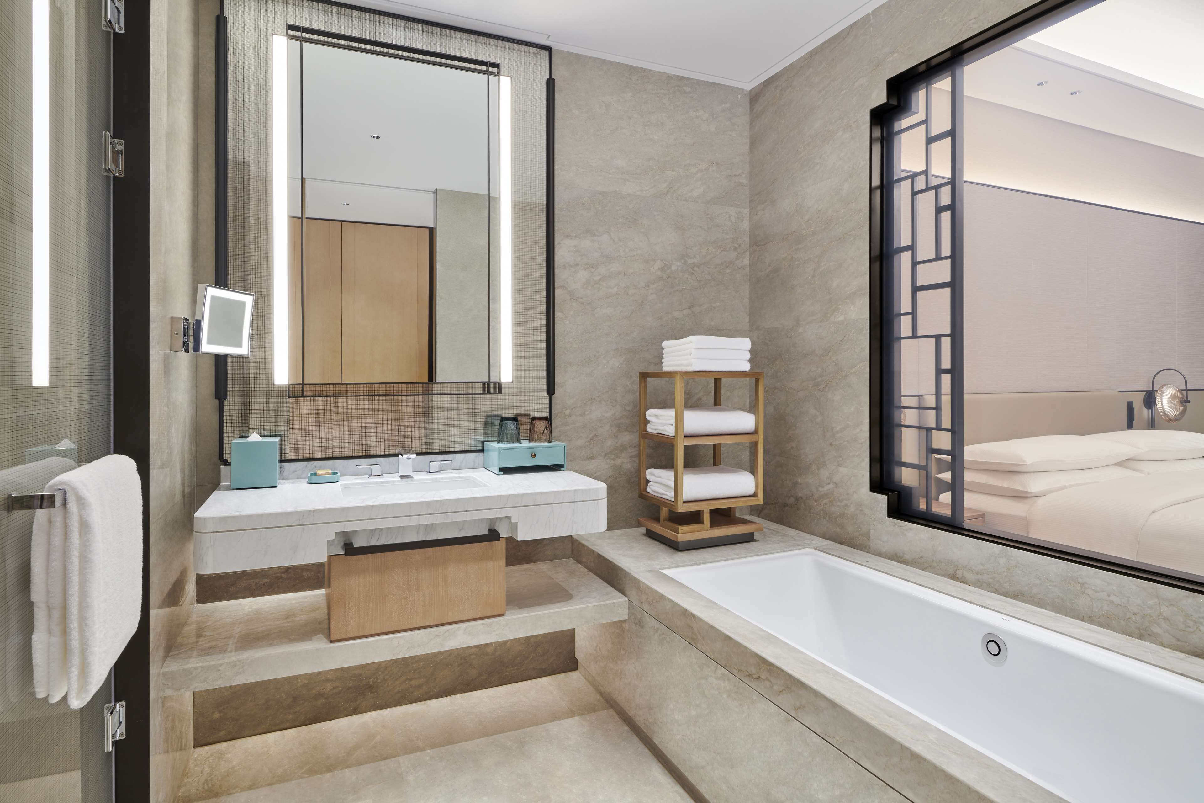 Un baño moderno con un espejo grande, una bañera y un estante de madera con toallas.