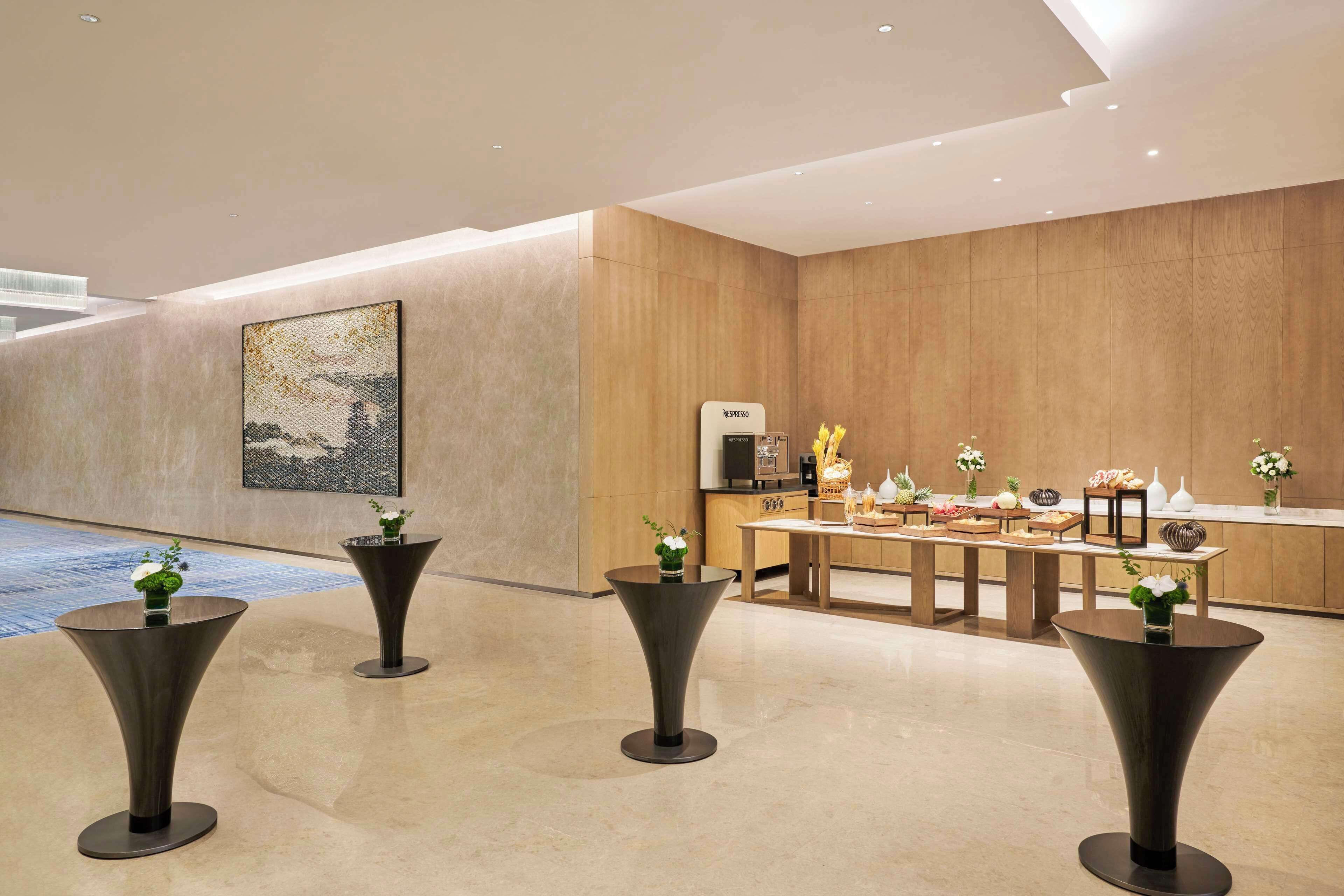 Un vestíbulo moderno de hotel con una recepción, un cuadro abstracto grande y tres mesas pedestal negras con jarrones.